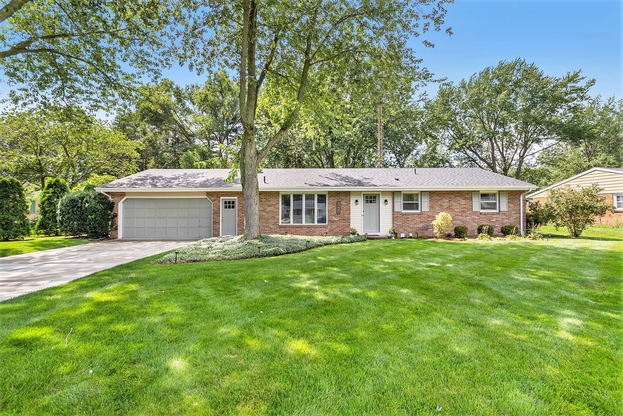 Single-story brick house with green lawn and trees