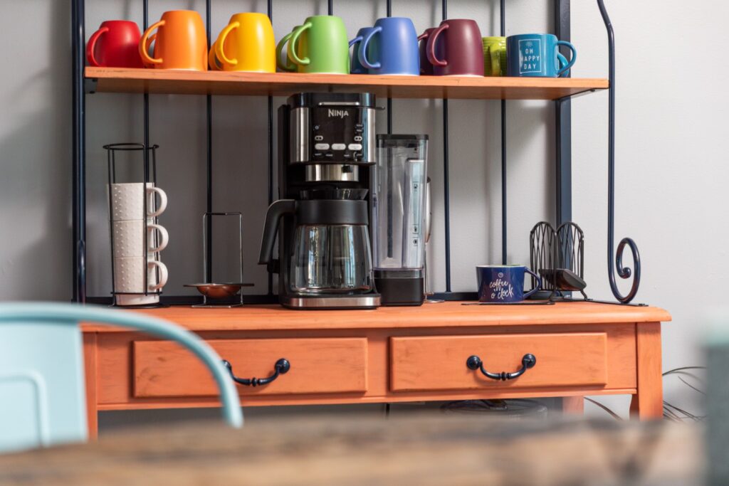 Coffee maker with colorful mugs on wooden shelf