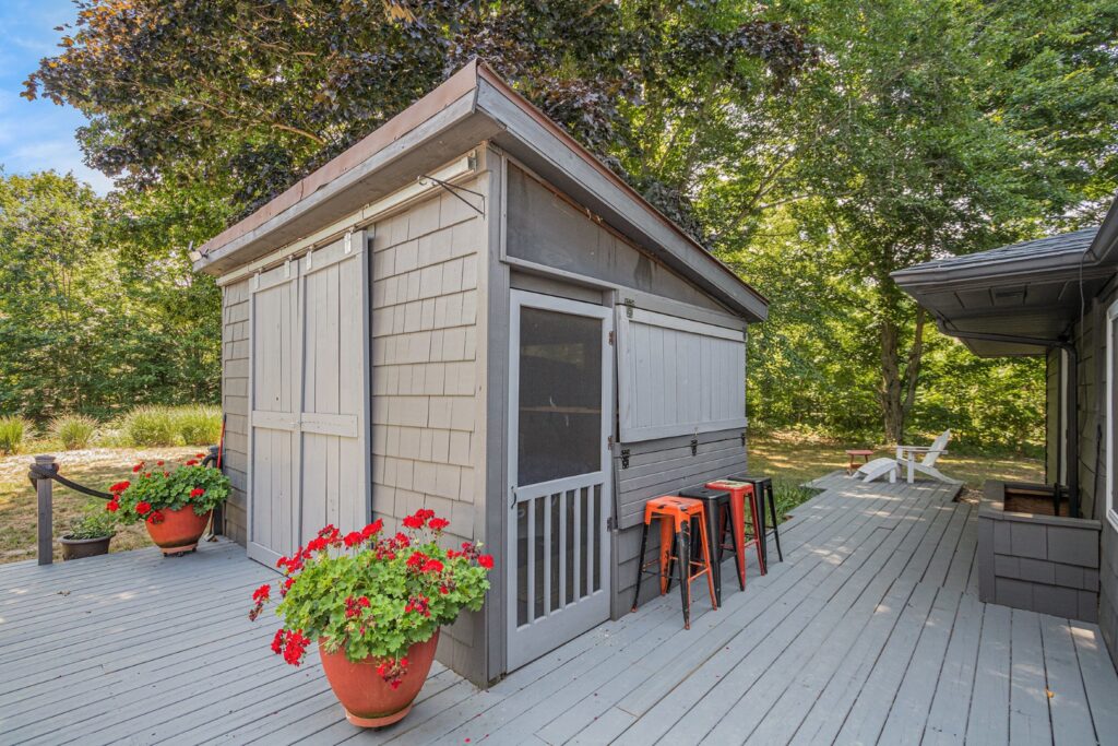 Gray backyard shed with patio and red flowers