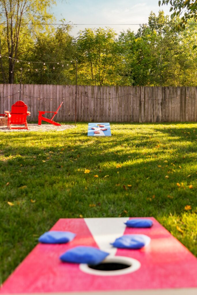 Backyard cornhole game with red chairs