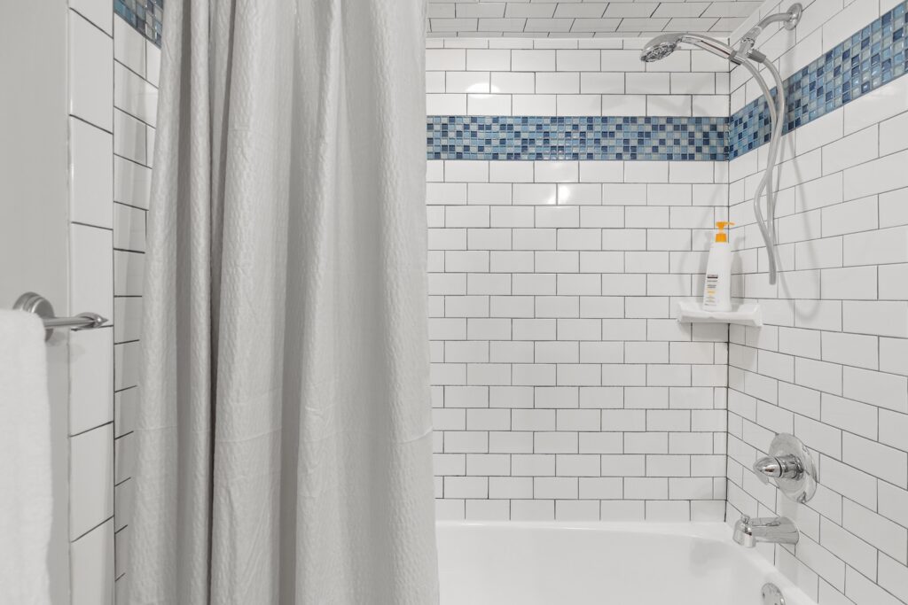 White tiled bathroom shower with curtain and shampoo bottle